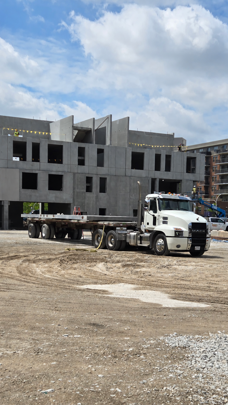 White Mack truck with a flatbed trailer at a construction site