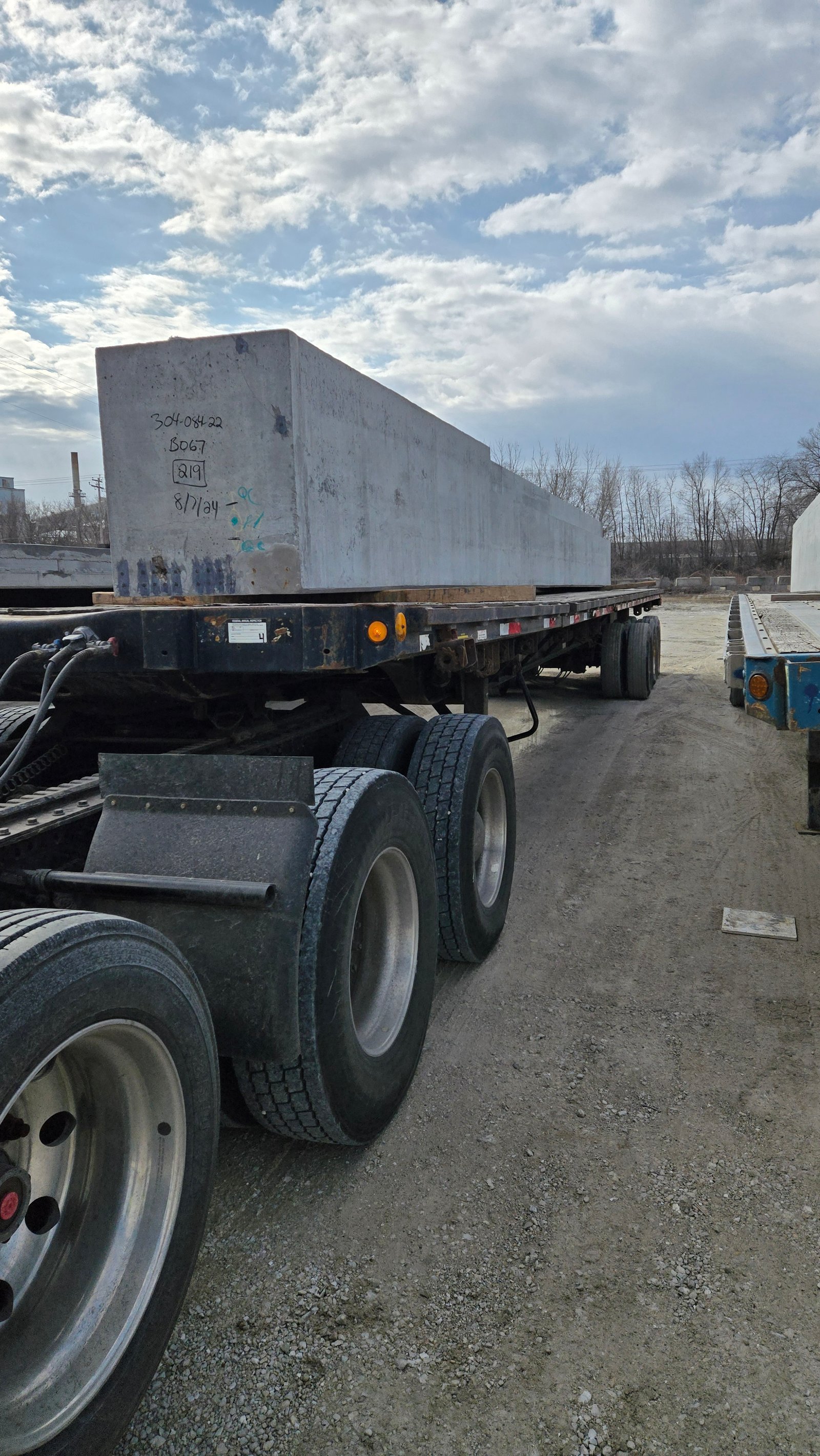 Large precast concrete section resting on a flatbed trailer in a materials yard